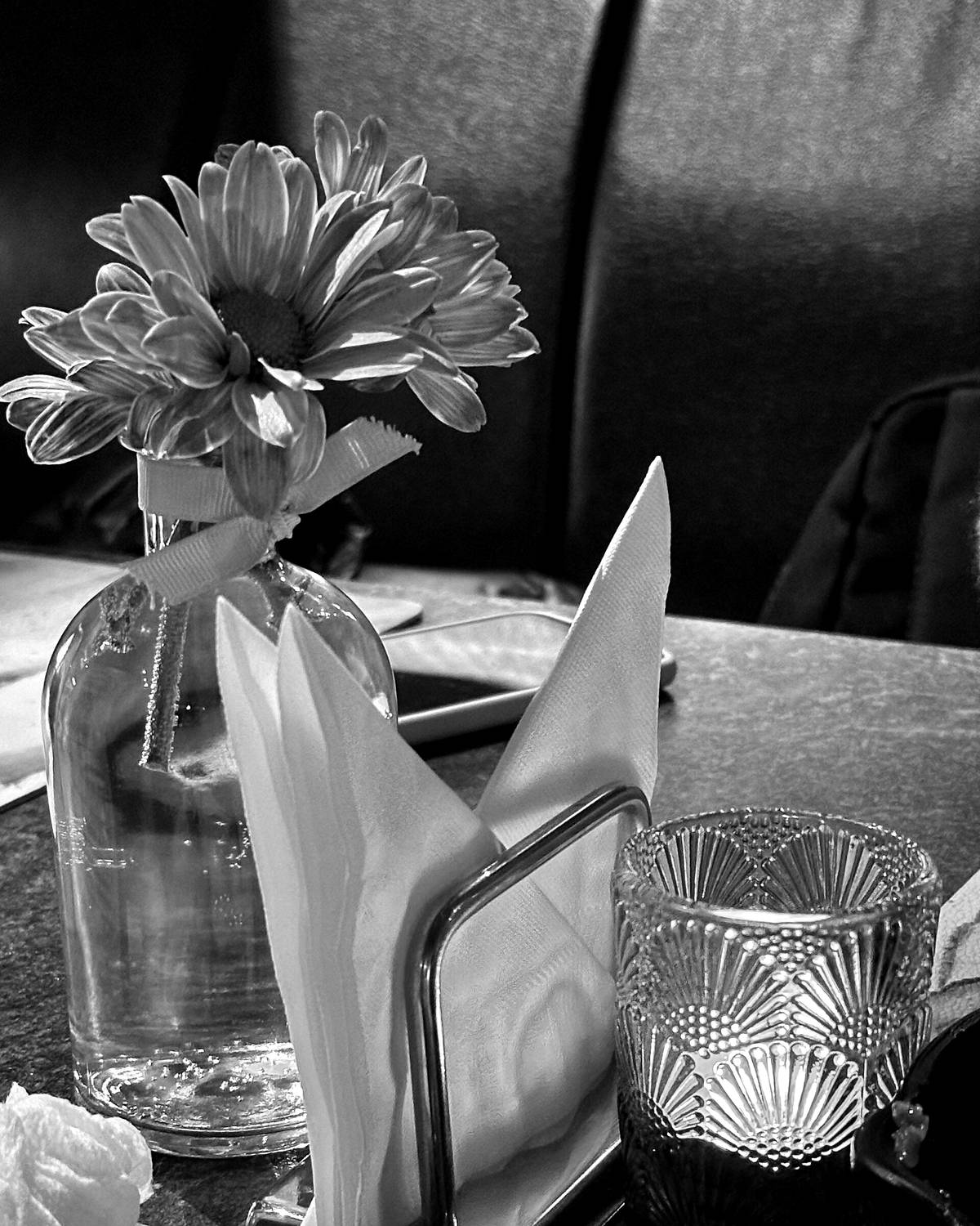 A single flower in a glass carafe beside folded napkins and a cut-glass tumbler on a café table